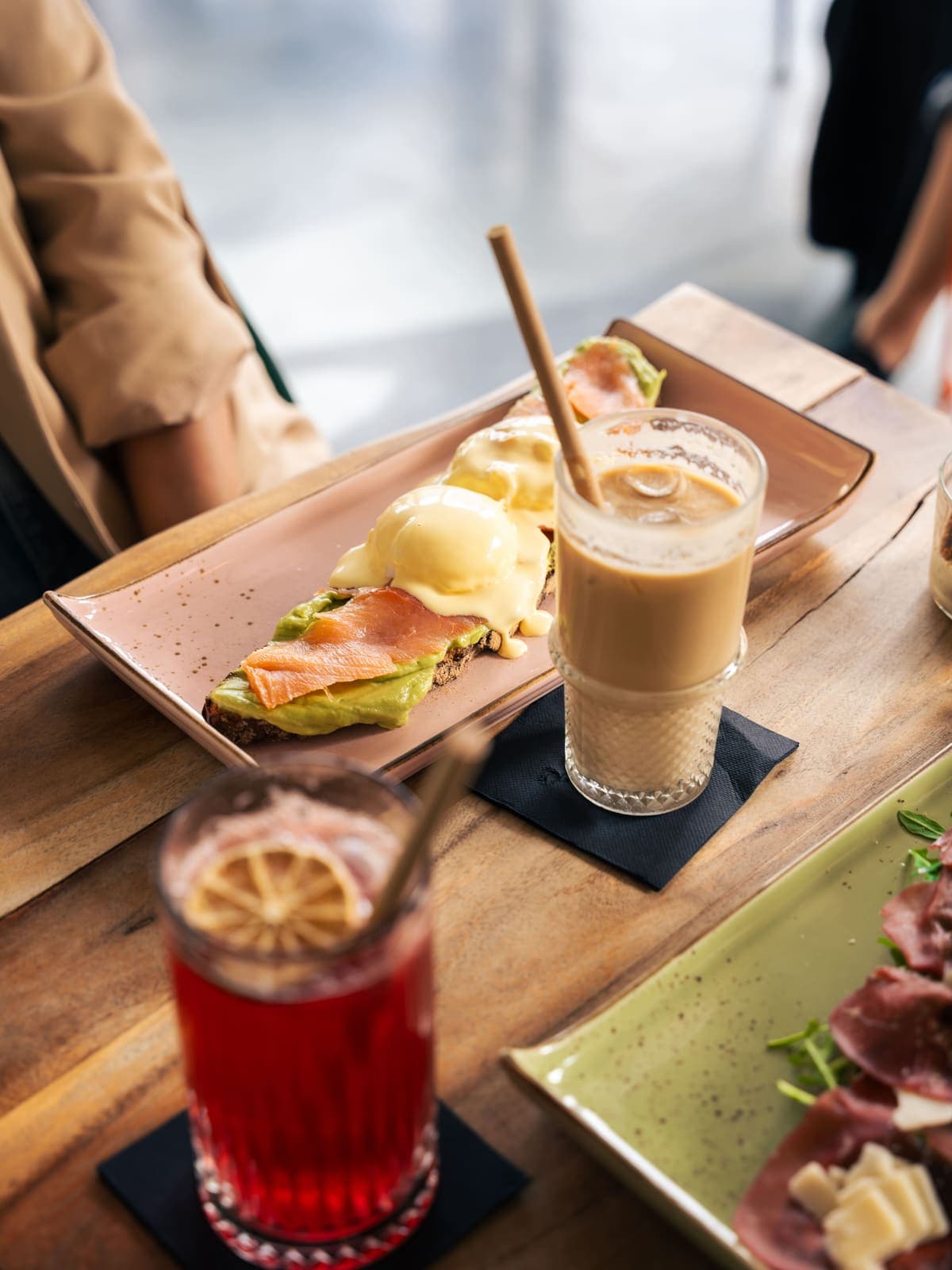 Pochiertes Ei mit Lachs und Avocado neben einem Iced Latte auf dem Holztisch im Café DOA